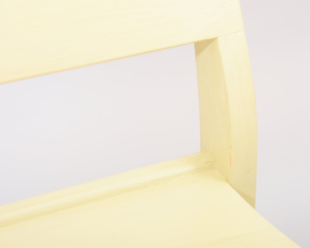 Front view showing a partial close-up of the Alvar Aalto 611 chair’s seat, frame, and backrest, all made of wood and painted light yellow.