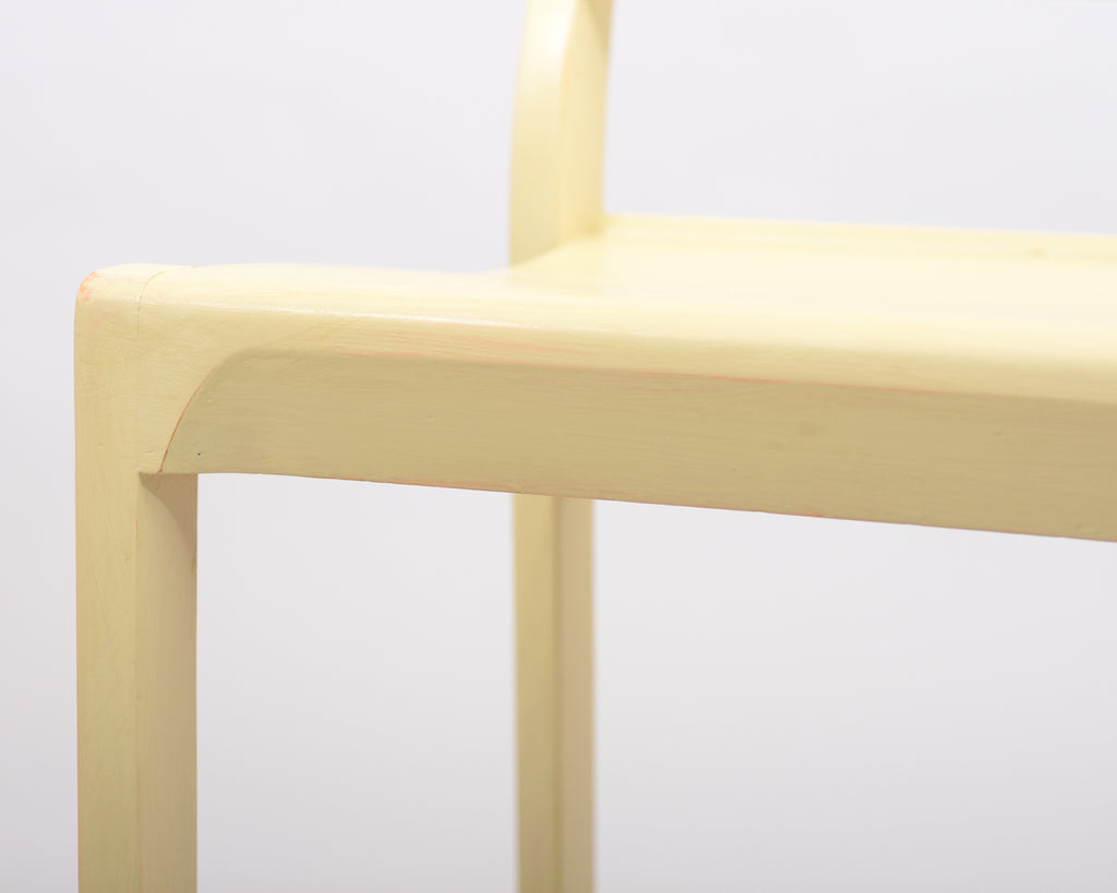 Close-up view of the front edge of the Alvar Aalto 611 chair’s seat, made entirely of wood and painted light yellow.