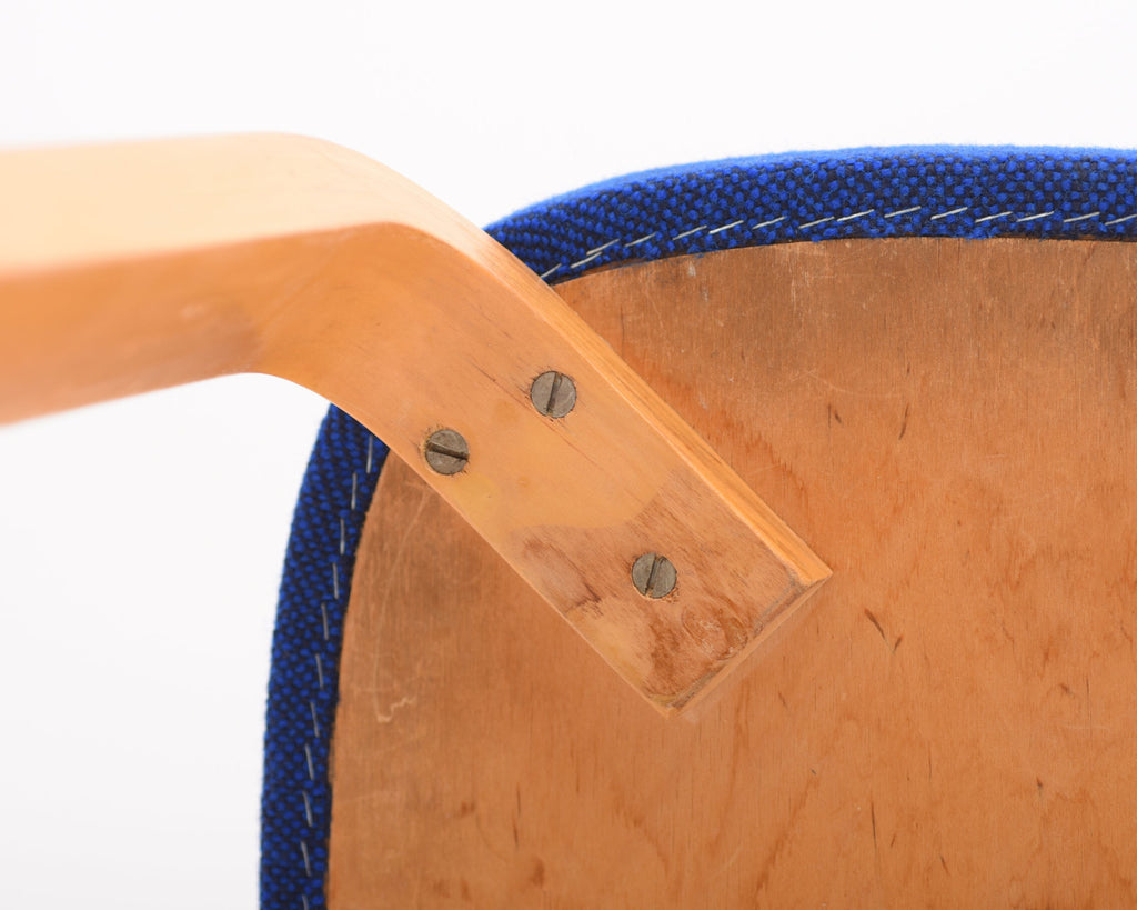 Close-up of the underside of the chair seat showing one leg attached with three old screws and the blue fabric upholstery fixed with staples.