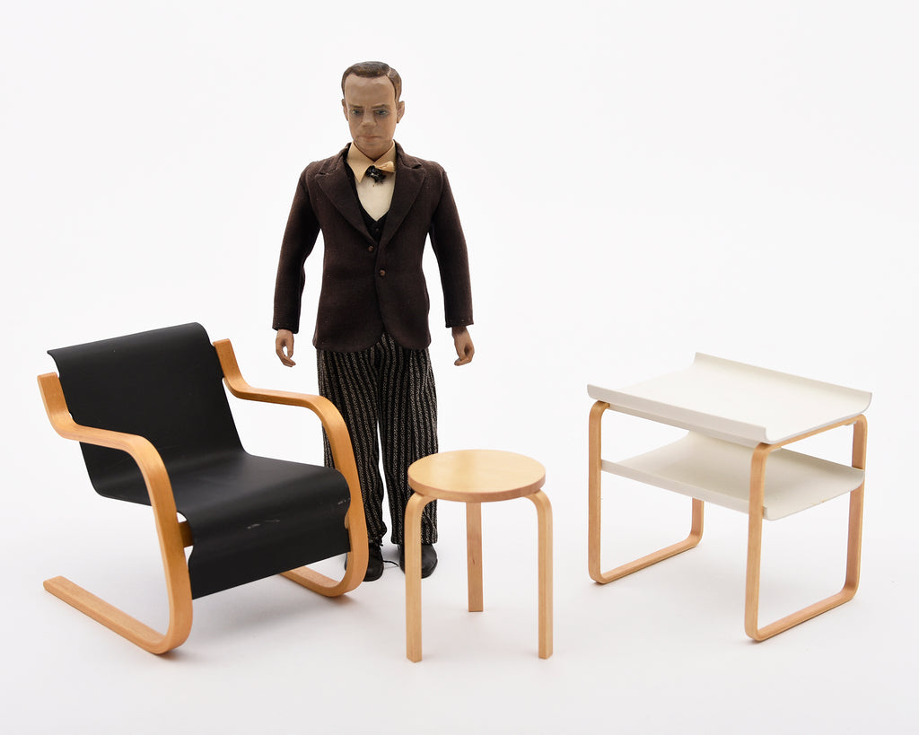 Figure in a suit standing next to modern furniture on a white background.