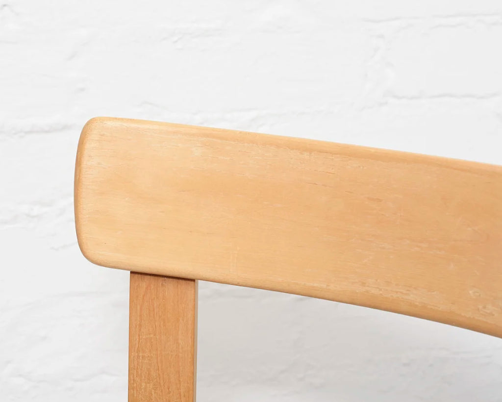 Close-up of the backrest of a wooden chair with a light finish on a white background.