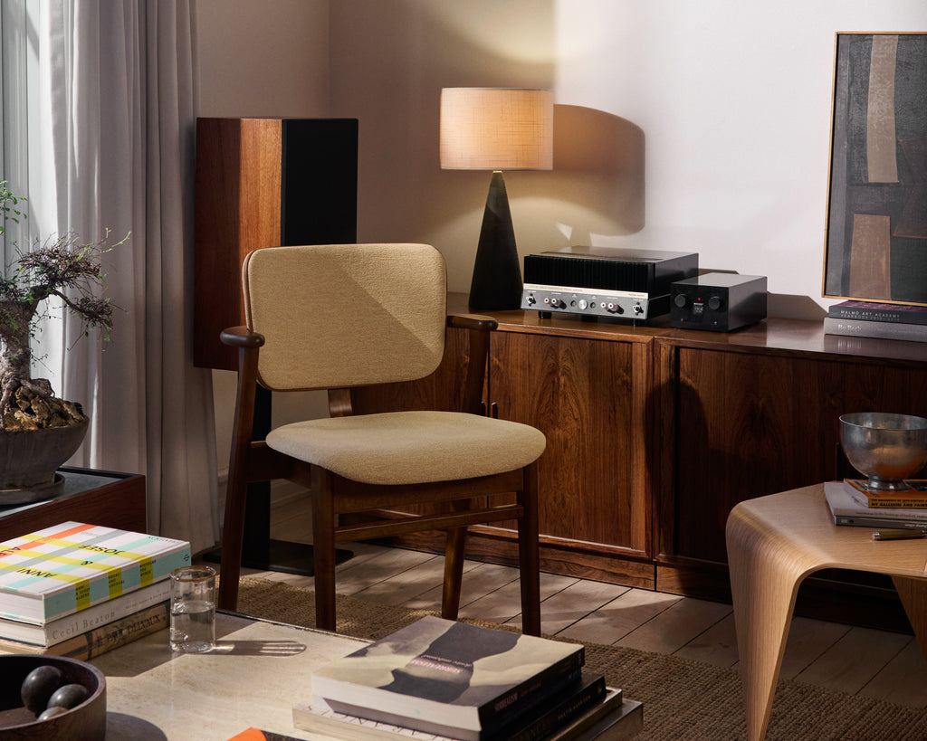 Domus Chair in walnut‑stained birch, upholstered in Wow Re beige‑pink fabric, shown in a layered living room.