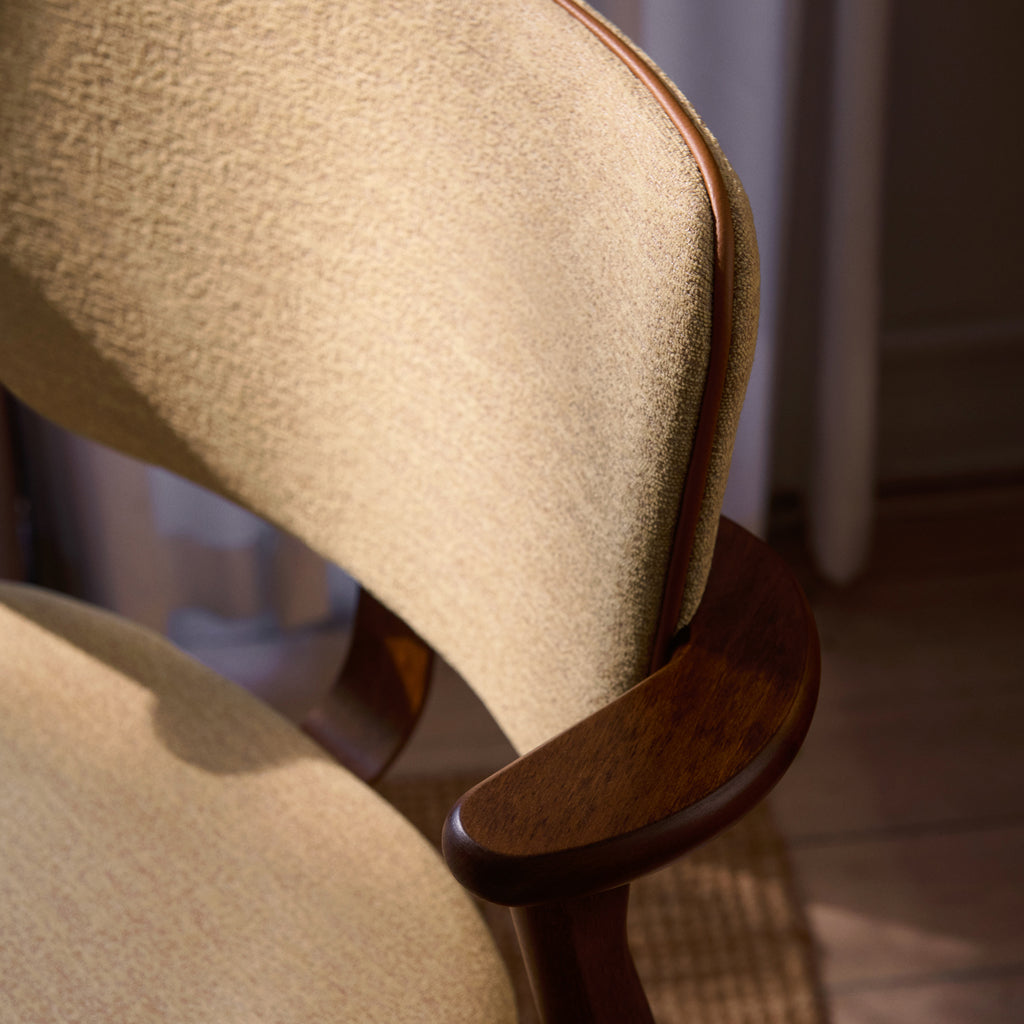Close‑up view of the Domus Chair’s backrest, highlighting the Prestige Cognac leather piping on the Wow Re beige‑pink upholstery and the walnut‑stained birch frame.