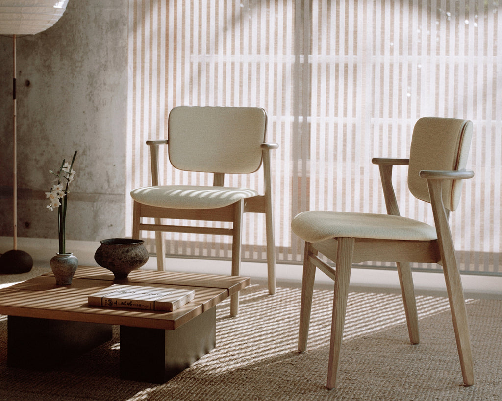 A Japandi‑style / minimal living room featuring two light‑toned Domus chairs with oak frames, upholstered in Wow Re cream‑white fabric with Prestige Nougat leather piping.