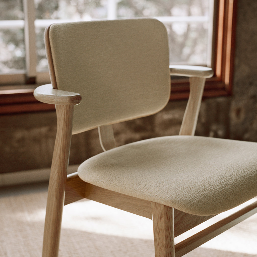 Close‑up view of the Domus Chair, showing the oak frame and the seat and backrest upholstered in Wow Re cream‑white fabric with refined Prestige Nougat leather piping.
