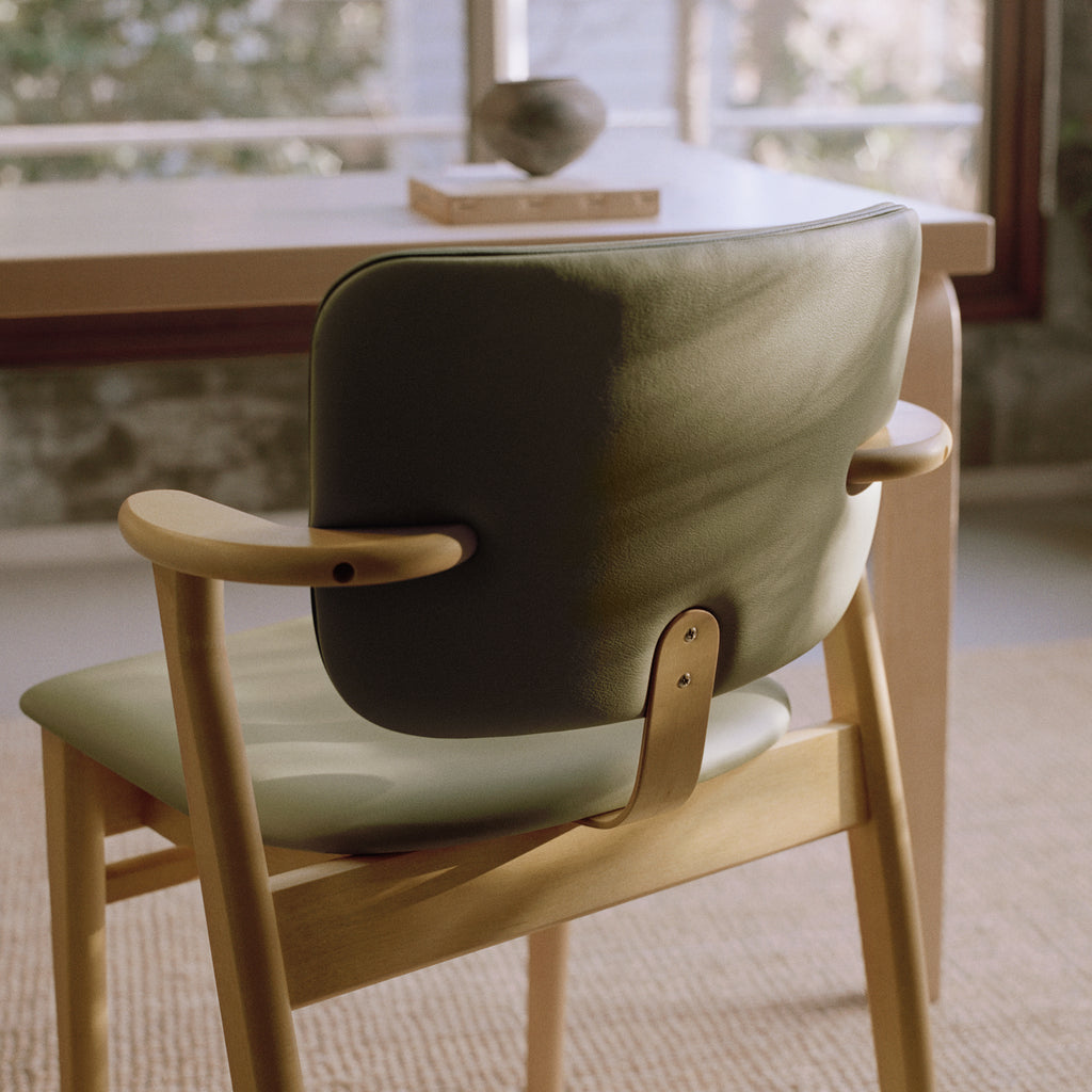 Close‑up rear view of the Domus Chair, showing the honey‑stained frame and the Spectrum Leaf leather upholstery with contrasting Spectrum Moss leather piping.
