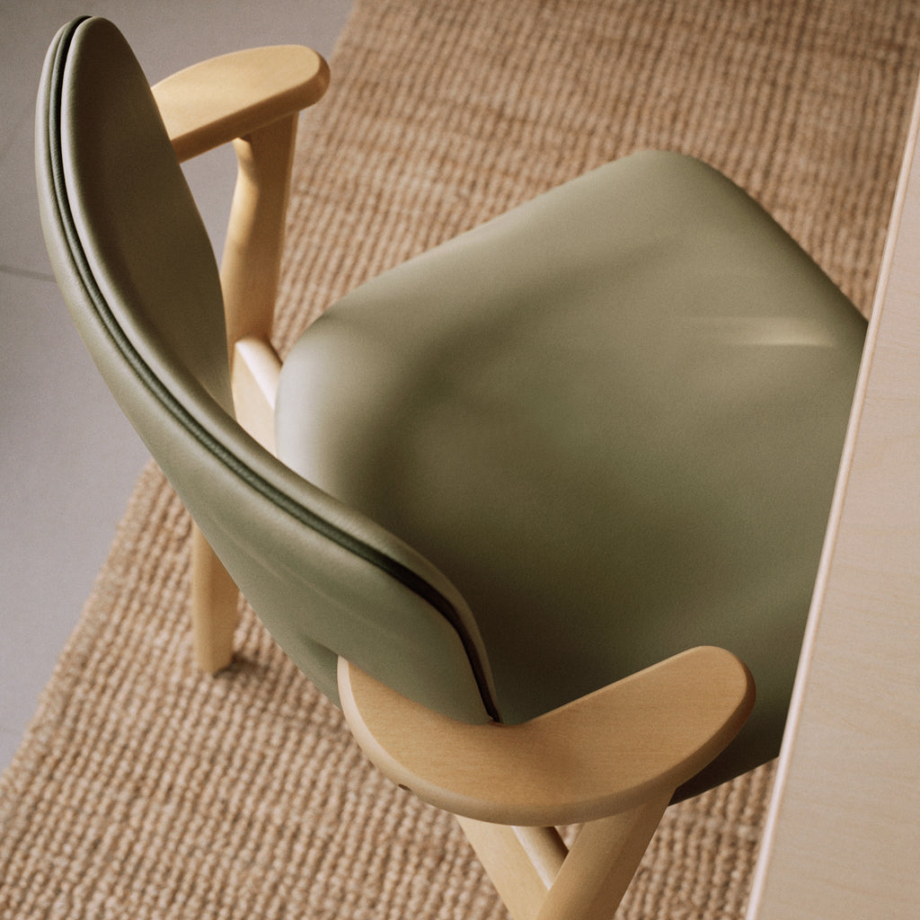 Top‑down close‑up of the Domus Chair, showing the backrest and seat upholstered in Spectrum Leaf leather with contrasting Spectrum Moss leather piping, on a honey‑stained birch frame.