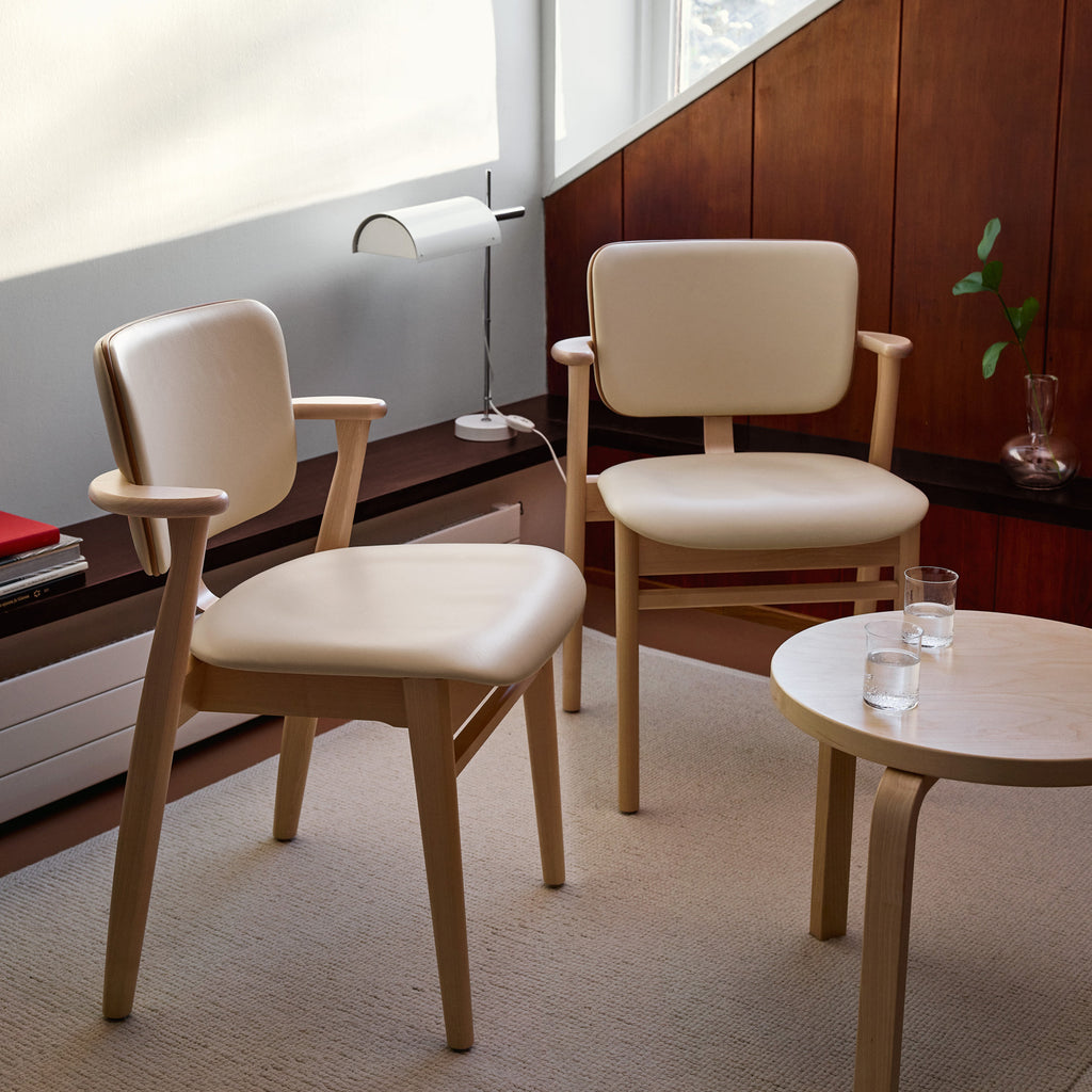 In a Nordic‑style living‑room corner, two Domus chairs upholstered in Prestige Cream leather are placed beside an Aalto 90D table.