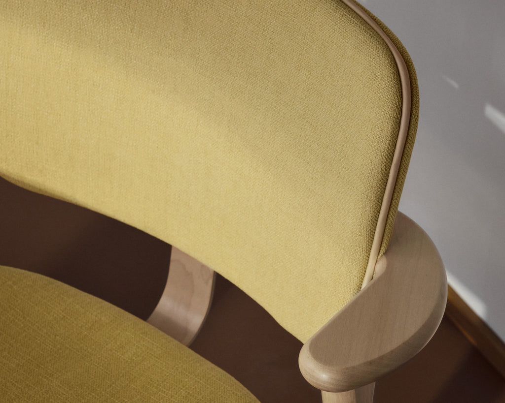 Close‑up front view of the Domus Chair, showing the backrest upholstered in light‑yellow Hola Canary fabric with finished Prestige Cream leather piping.