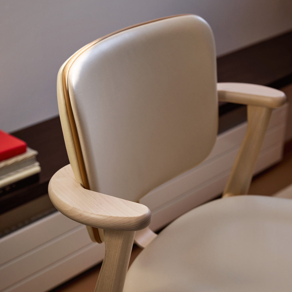 Side‑angled view of the Domus Chair, highlighting the clear‑lacquered birch frame, the backrest and seat upholstered in Prestige Cream leather, and the refined Prestige Nougat leather piping.