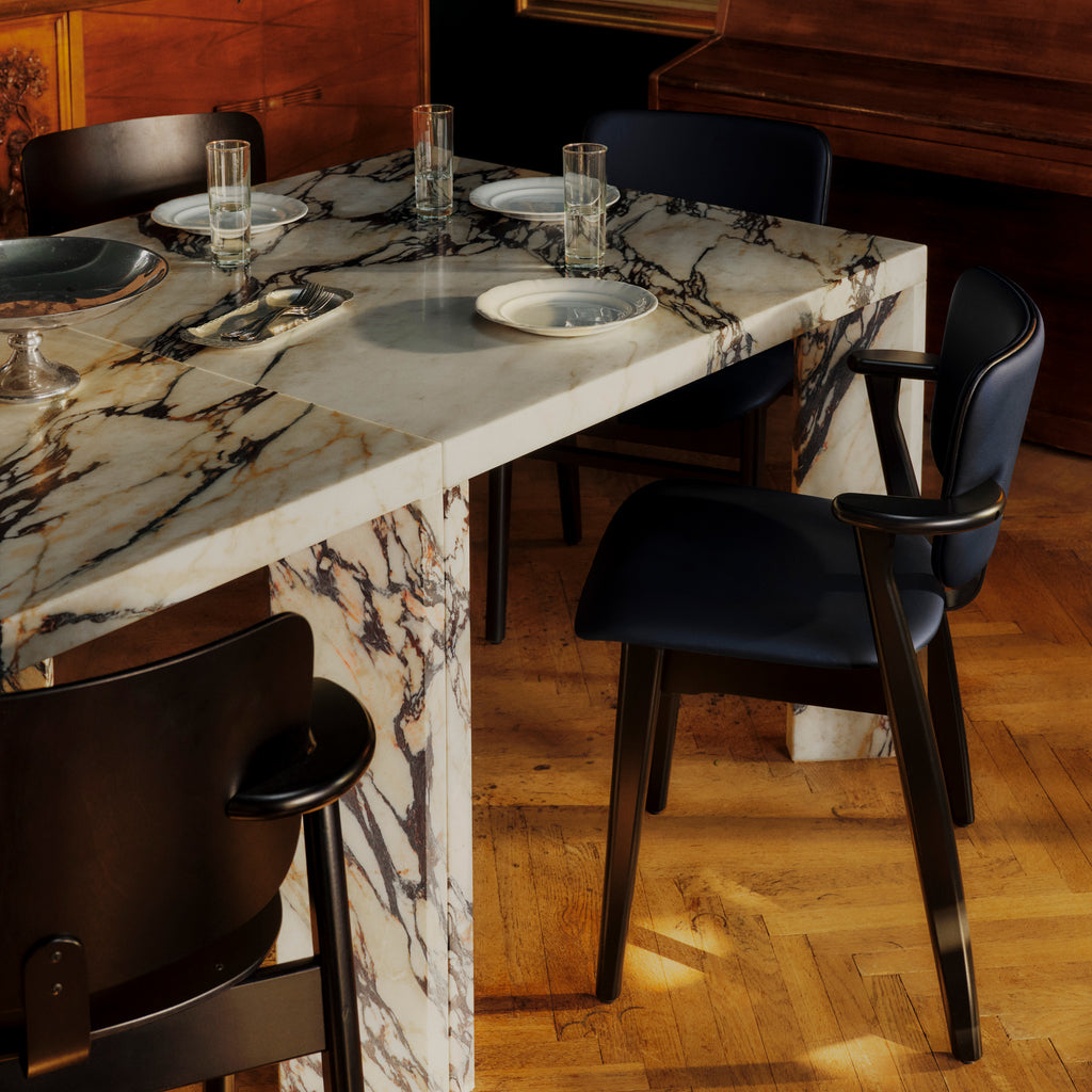 An opulent dining room featuring a grand marble table surrounded by black‑stained Domus Chairs upholstered in Spectrum Marine leather with matching Prestige Black leather piping.