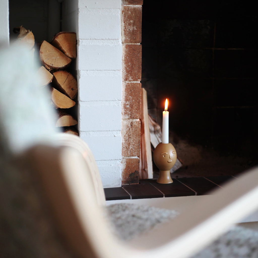 Close-up photograph of a Lucius candle holder placed on a fireplace mantel. A single candle is lit.