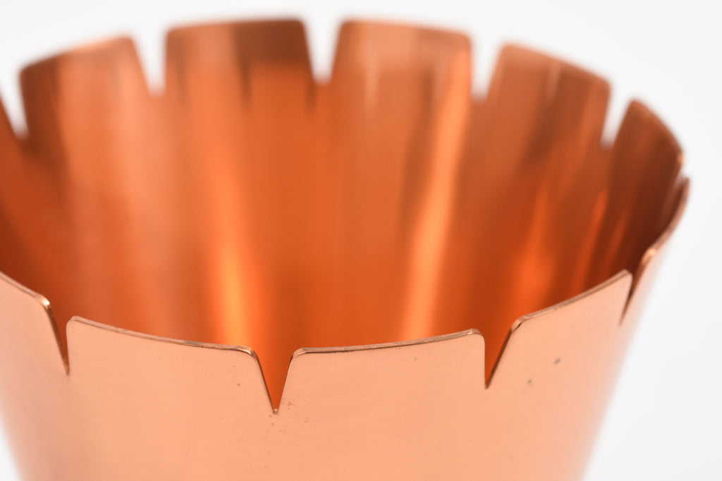 Close-up of a copper-colored metal object with a scalloped edge on a white background.