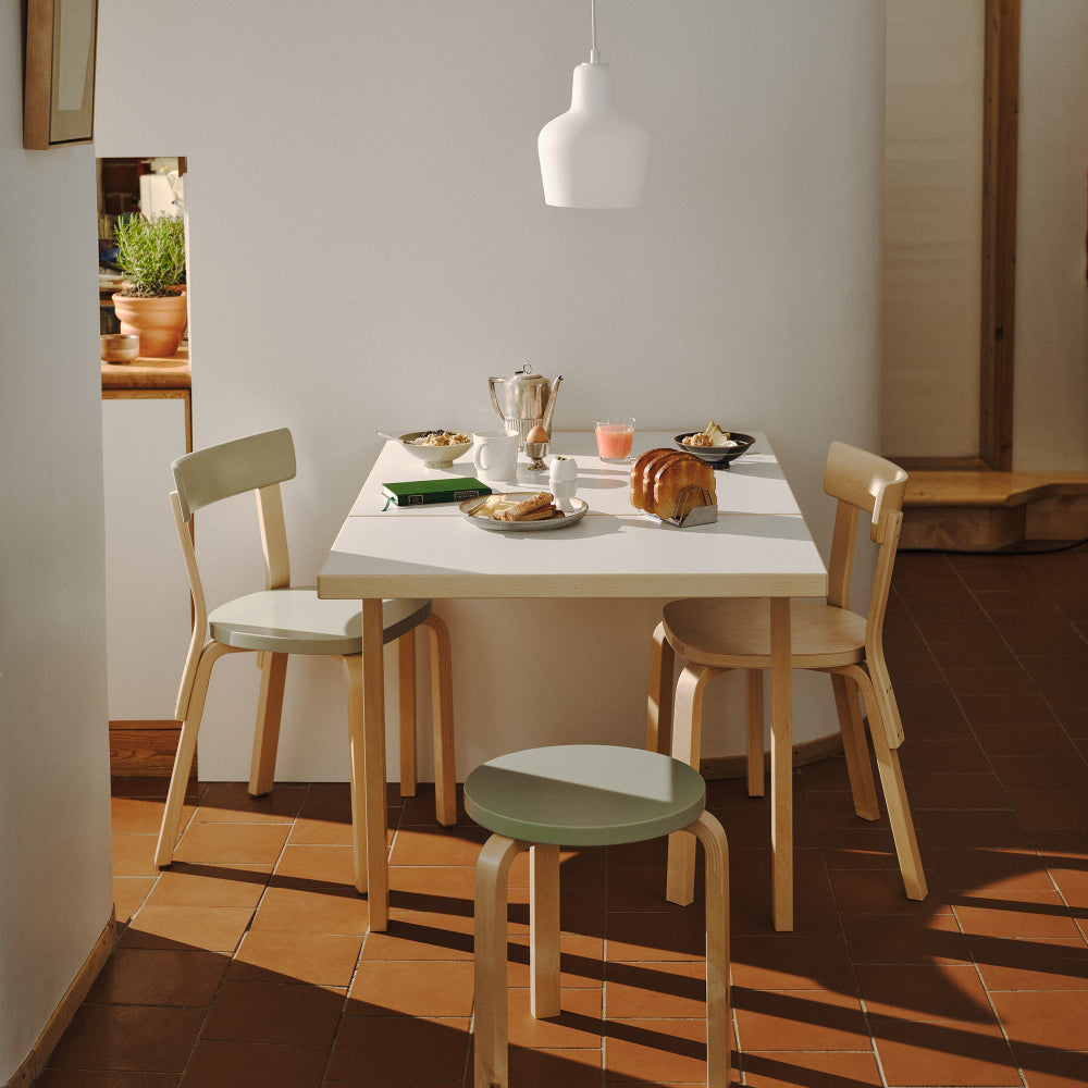 Interior view of a small dining area next to a kitchen, featuring Aalto Foldable Table DL81C with a white laminate top. Two Chair 69 and one Stool 60 are placed around the table, with Pendant Light A440 hanging above.