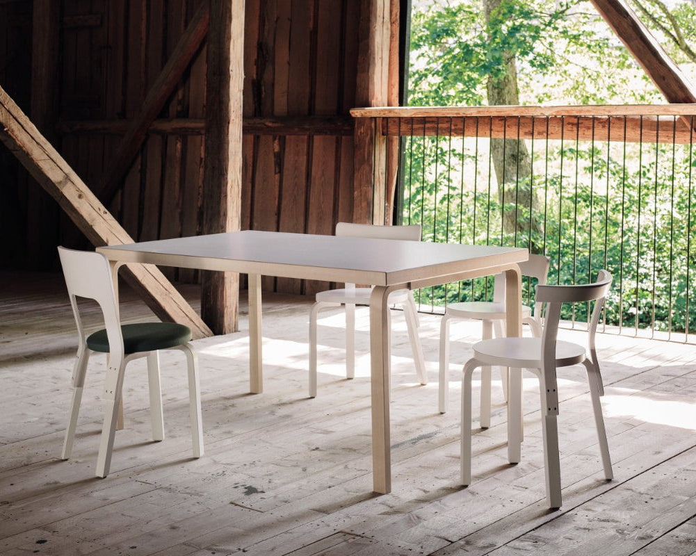Interior view of a dining group located in a barn, featuring rectangular Aalto Table 82A with a white laminate top surrounded by Chairs 65, 66, 68 and 69.