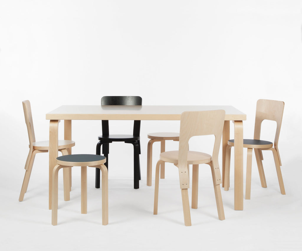 Interior view of a white space featuring Aalto Table 82A with a white laminate top surrounded by different versions of Chair 66. Also, two Stool 60 are also placed around the table.