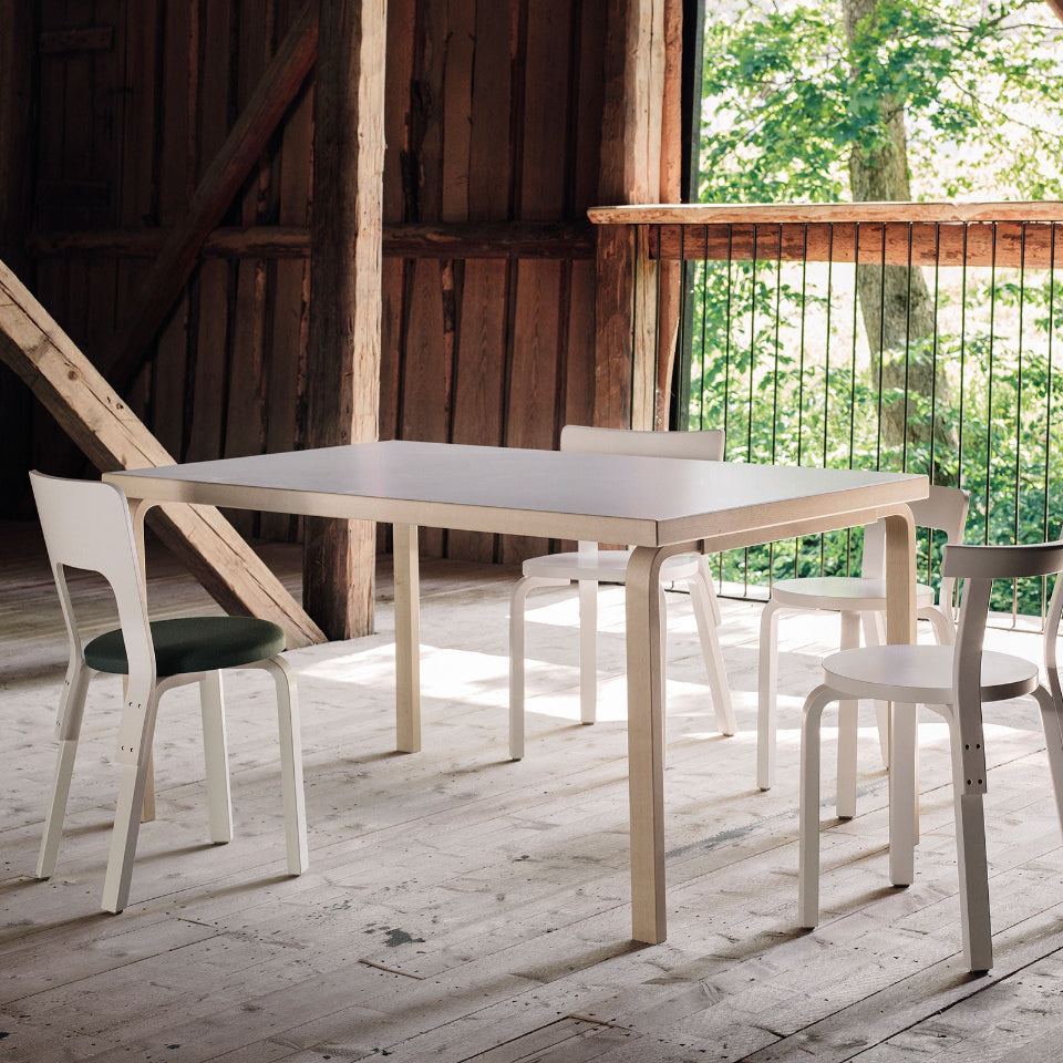 Barn interior featuring Artek Aalto Table 82A with a white laminate top. The table is surrounded by four white chairs in different models: Chair 65, Chair 66, Chair 68, and Chair 69.