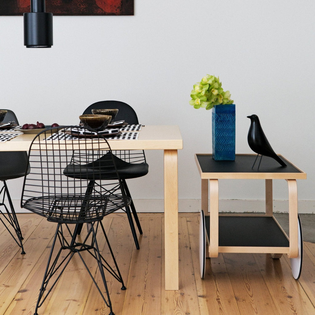 Dining area featuring Aalto Table 82B surrounded by chairs. A Tea Trolley 901 is placed at the end of the table, and a fully black Pendant Light A110 “Hand Grenade” is positioned above the table.