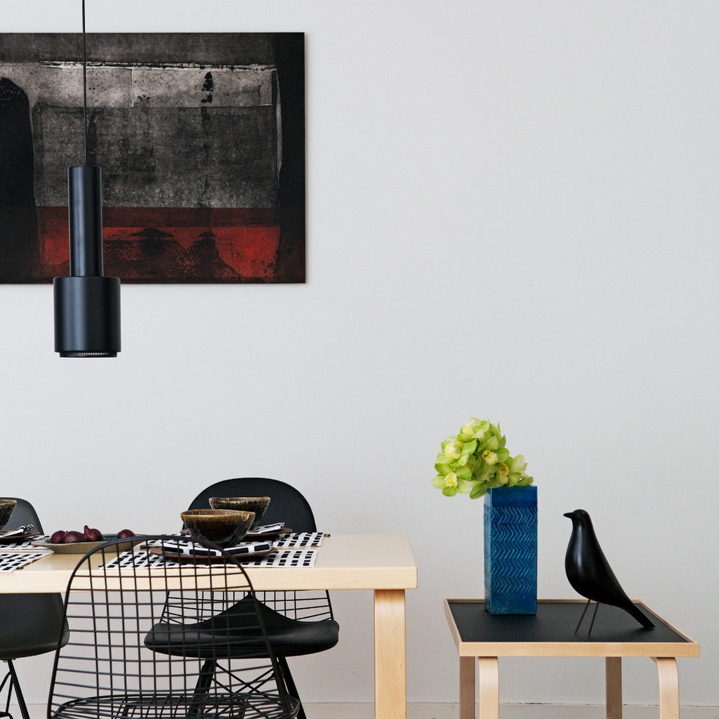 Dining area featuring Aalto Table 82B surrounded by chairs. A Tea Trolley 901 is placed at the end of the table, and a fully black Pendant Light A110 “Hand Grenade” is positioned above the table.