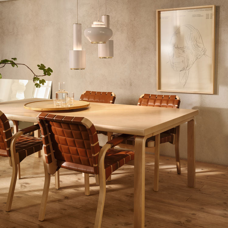 Interior view of a dining area featuring Aalto Table 83 surrounded by Armchair 45. Two Pendant Light A110 “Hand Grenade” and one Pendant Light A333 “Turnip” are positioned above the table.