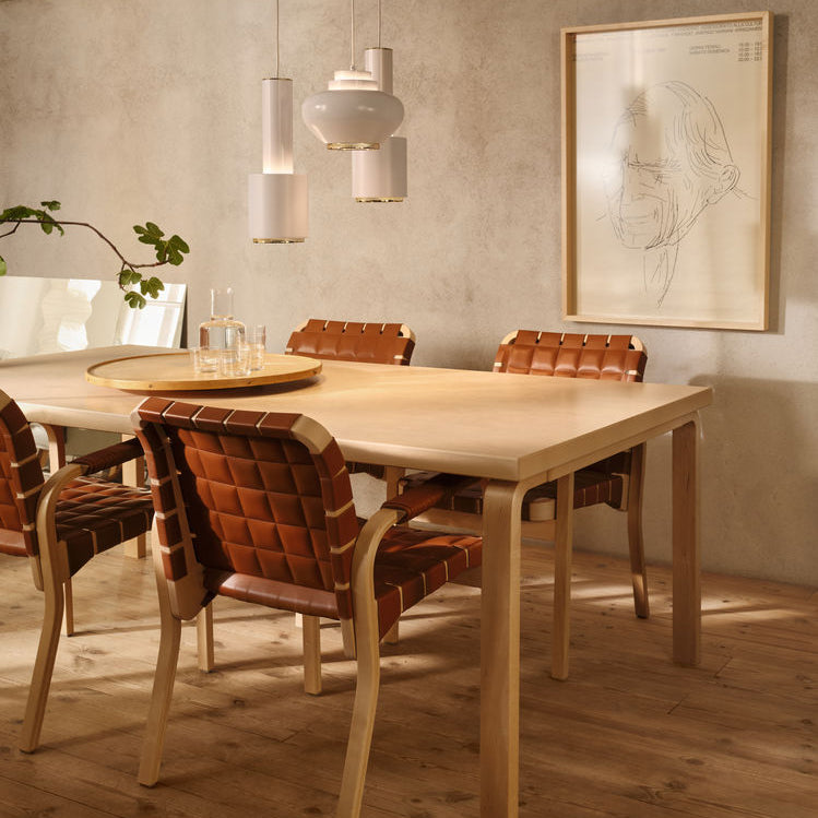 Interior view featuring Aalto Table 83 surrounded by four Armchair 45 upholstered in cognac leather. Two white pendant lights, A110 “Hand Grenade” and A333 “Turnip”, are placed above the table.