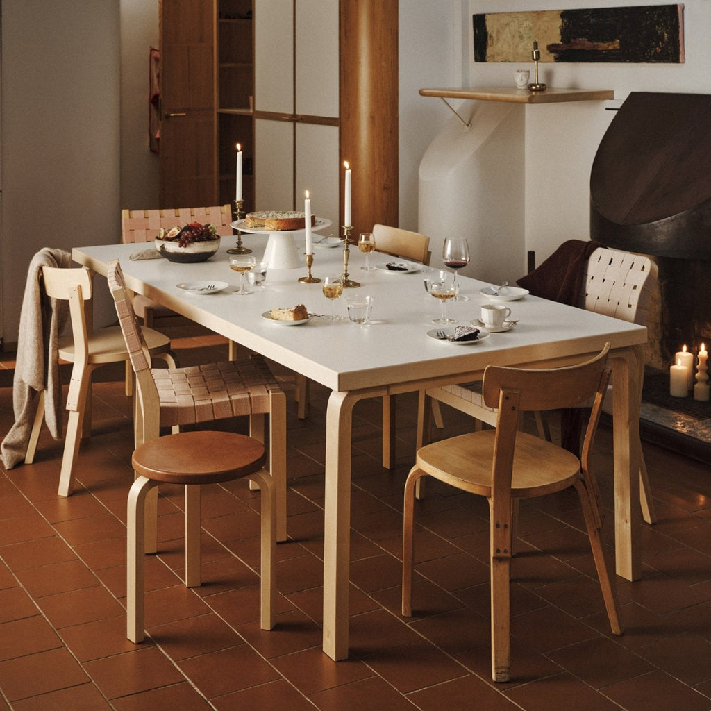 An atmospheric dining setting with an Aalto Table 86 surrounded by Chair 69, Chair 611 and Armchair 45. The table is styled with candles and a cake setting.
