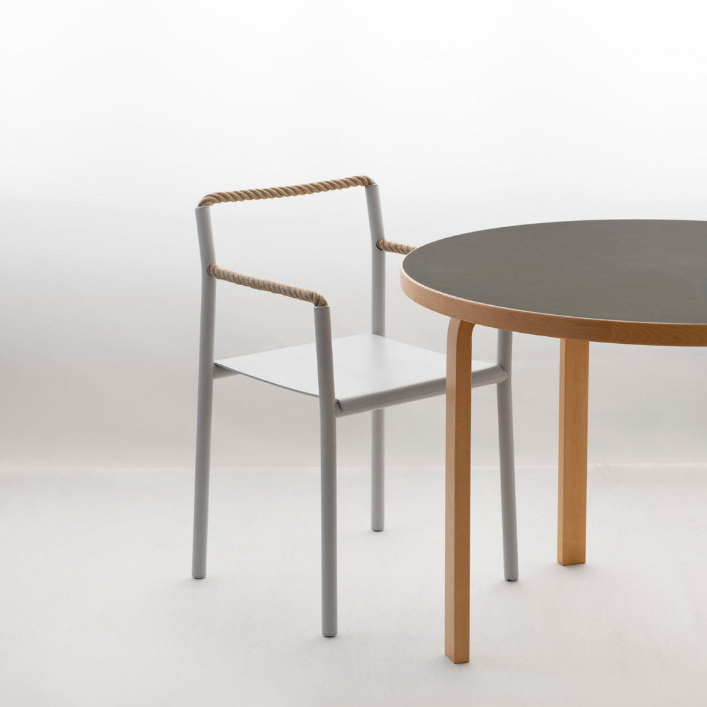 Minimalist interior featuring a white, open space with Aalto Table 90A with black linoleum top. A single Rope Chair is positioned beside the table.