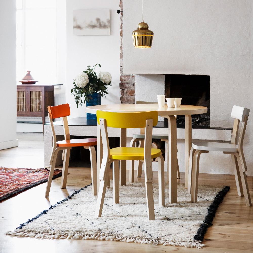 Dining area featuring a round Aalto Table 90A surrounded by four Chair 69. A fireplace is positioned behind the table, creating a warm and inviting setting. Pendant Light A330 hangs above the table.