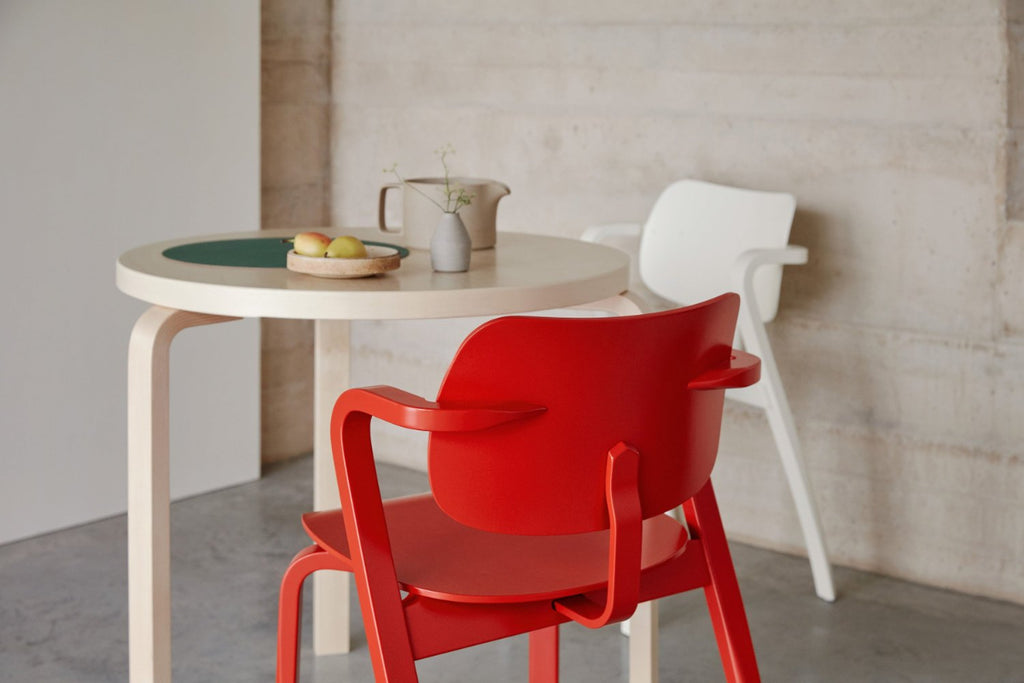 A round Aalto Table 90B surrounded by two Aslak Chairs in red and white.