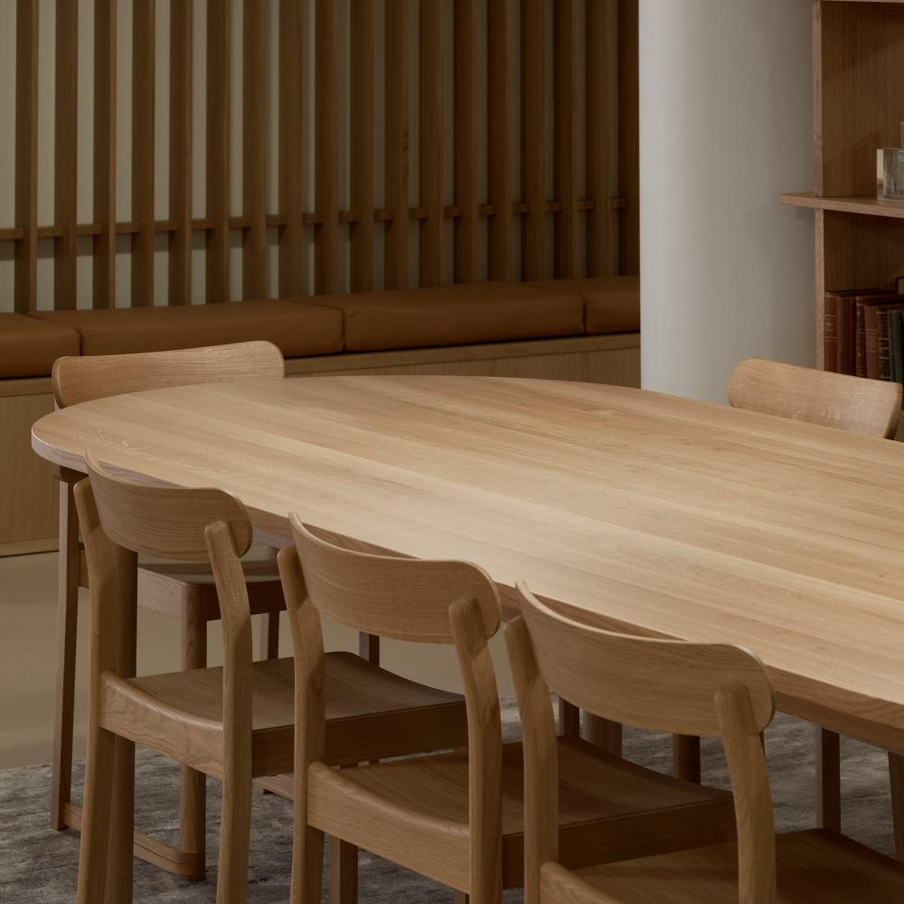 Interior view of an oval dining table surrounded by oak Atelier Chairs, creating a warm dining setting.