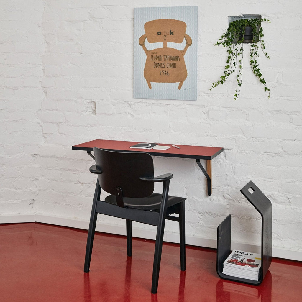 Interior view featuring a white brick wall with a Kaari Wall Console mounted on it, paired with a black Domus Chair. Kanto magazine rack is placed alongside.