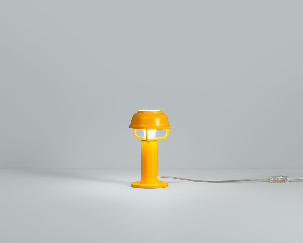 Product image of orange Artek Kori Table Light. The table light is switched on and photographed against a grey background.