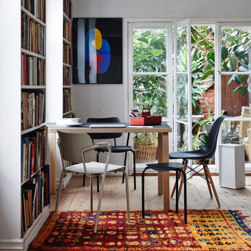 Dining area featuring a rectangular Aalto Table 81B surrounded by two Lukki Chairs. A large bookcase stands beside the table, and a tall window behind it opens views to a lush garden, bringing greenery into the space.
