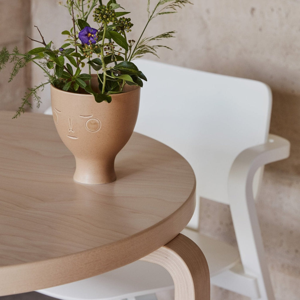 A close-up of a Midsummer Dream Vase with flowers on a round Aalto Table 90B, with a white Aslak Chair visible in the background.