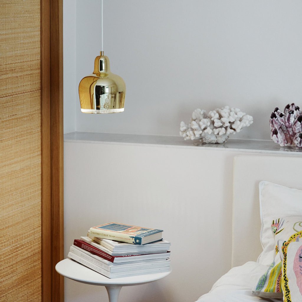 Interior view of a bedroom where a brass A330S Pendant Light “Golden Bell” is placed above a bedside table.