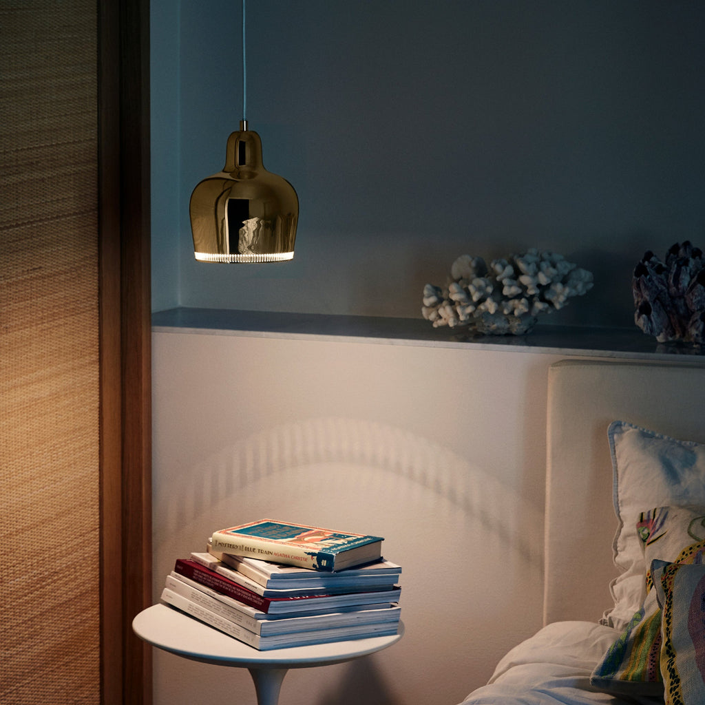 Interior view of a dimly lit bedroom where a brass A330S Pendant Light “Golden Bell” hangs above a bedside table.