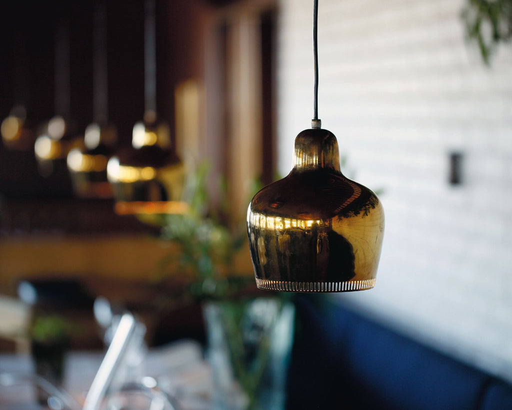 Close-up image from Savoy Restaurant in Helsinki, focusing on a brass Artek Pendant Light A330S “Golden Bell”. Additional pendant lights are visible in a row in the background, softly out of focus.