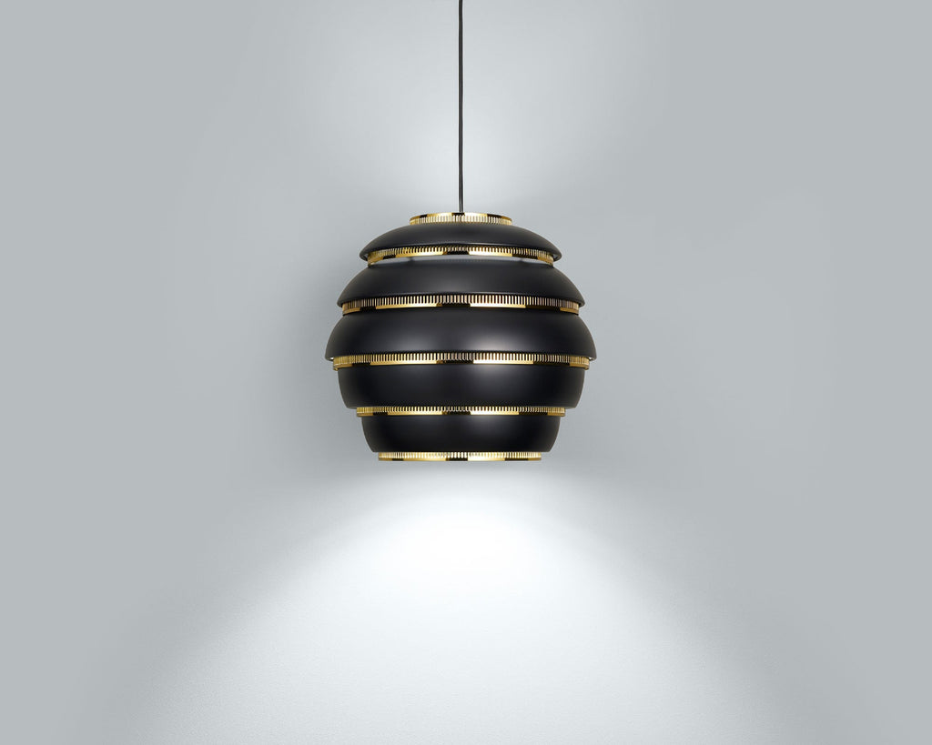 Product image of black Artek Pendant Light A331 “Beehive” with brass details. The pendant light is switched on and hangs against a grey background.
