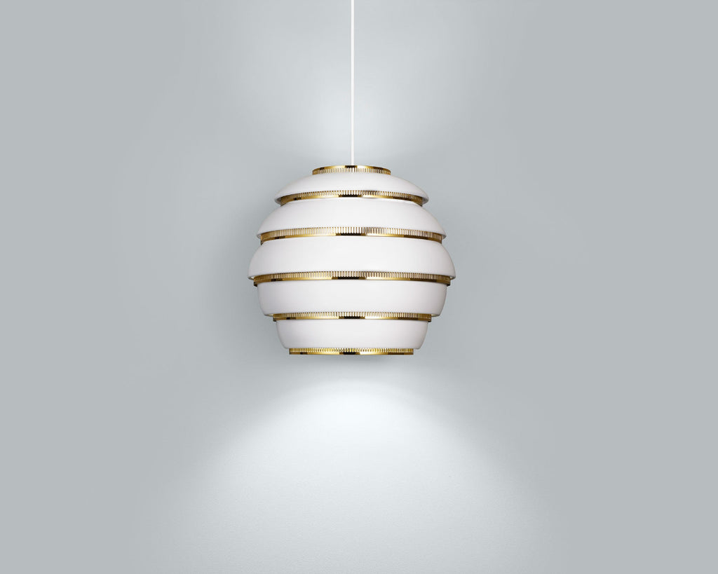 Product image of white Artek Pendant Light A331 “Beehive” with brass details. The pendant light is switched on and hangs against a grey background.