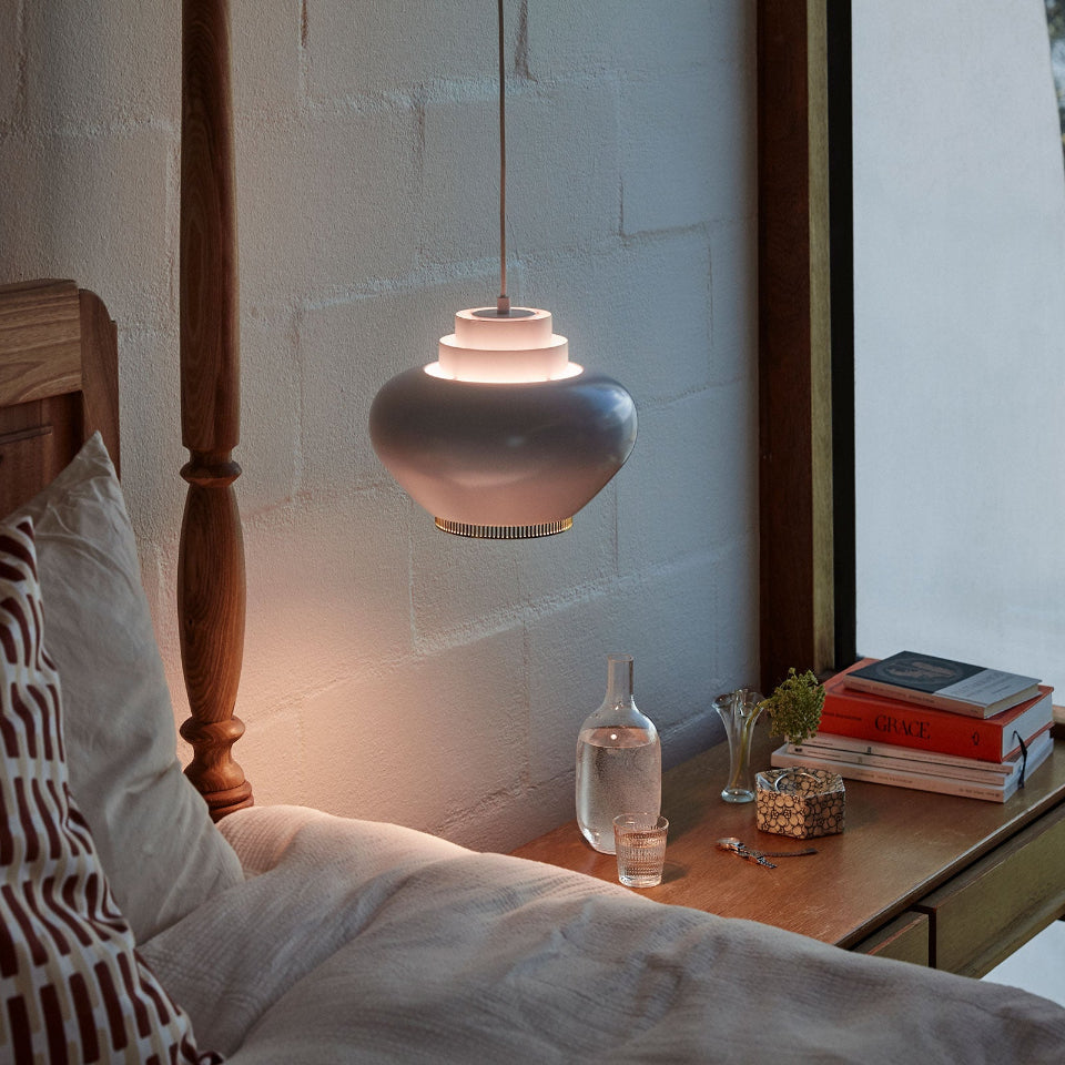 Pendant Light A333 “Turnip” hanging above a bedside table in a bedroom at dusk. The pendant light is switched on, casting a warm glow in the softly lit space.