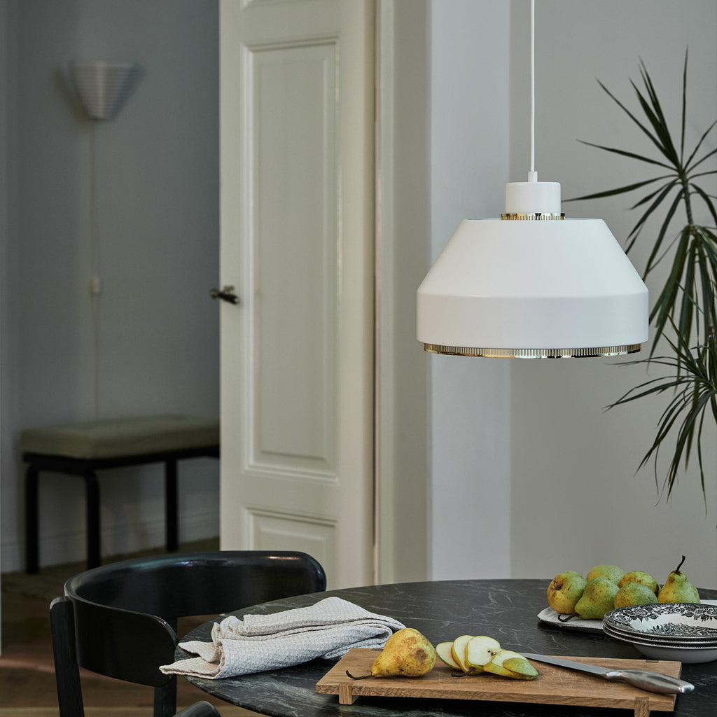 Interior view of a dining area lit by daylight, featuring AMA500 Pendant Light switched off above the table. In the background, an entry space reveals Bench 153B and Wall Light A910.