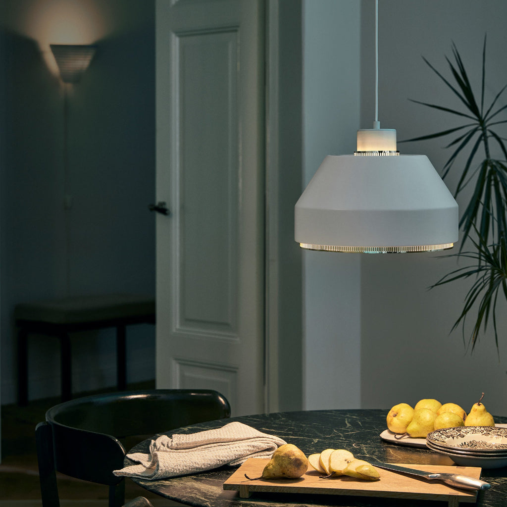 Interior view of a dimly lit dining area featuring a white AMA500 pendant light switched on above a dining table.