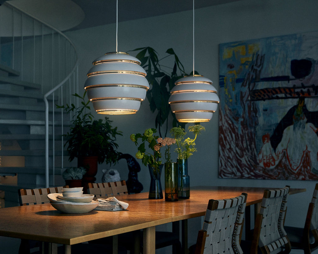 Atmospheric dining space lit only by lighting, featuring a vintage Artek dining set. Two white Pendant Light A331 “Beehive” with brass details hang above the table. 