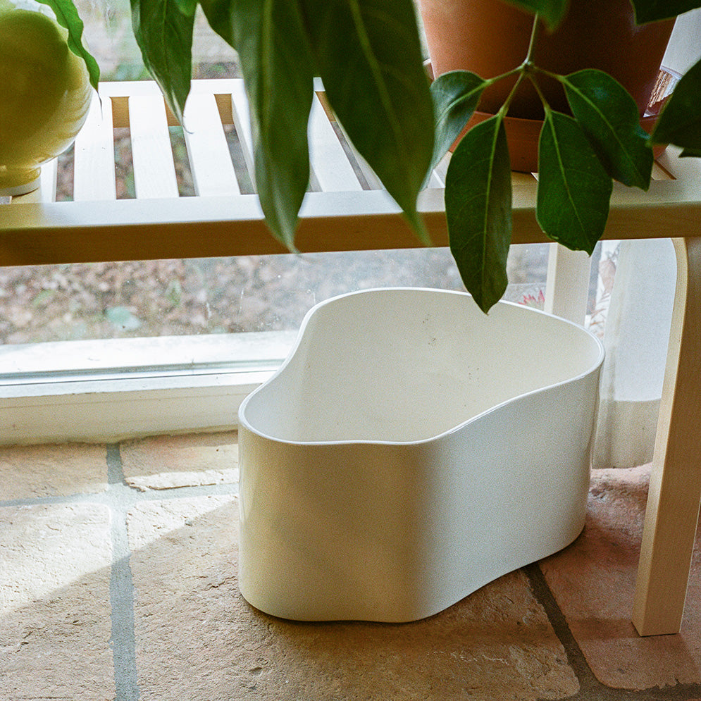 Interior view featuring a birch Bench 153A with a slatted top. Plants are placed on top of the bench, while a white Riihitie Plant Pot A is positioned underneath.