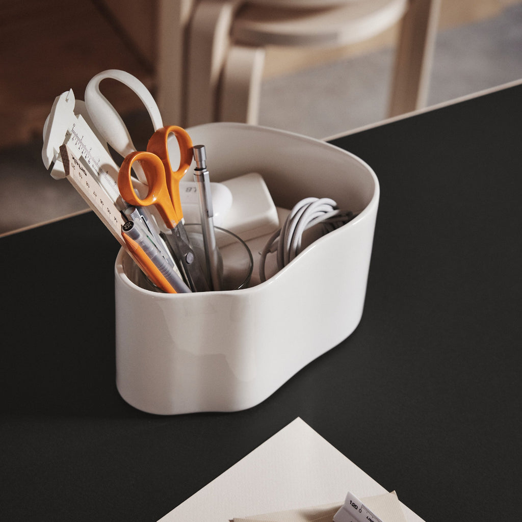 Close-up interior view featuring Riihitie Plant Pot A in white placed on a desk, holding pencils, rulers, scissors and a charging cable.