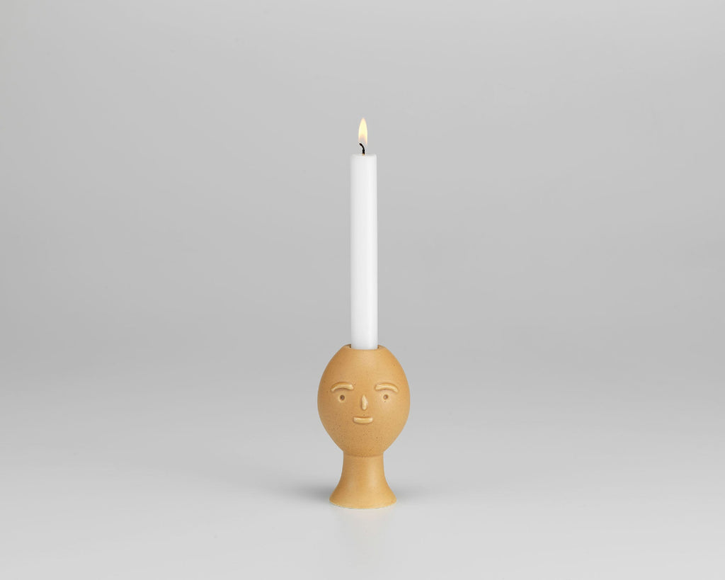Product image of Artek Secrets of Finland Lucius Candleholder with one lit candle, photographed against a grey background.