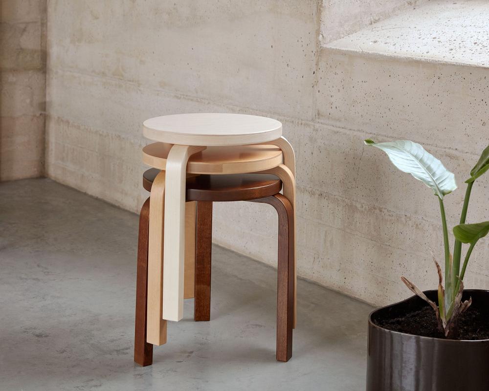Minimalist interior featuring three Artek Stool 60 stacked together. The stools are finished in birch, honey stain, and walnut stain.