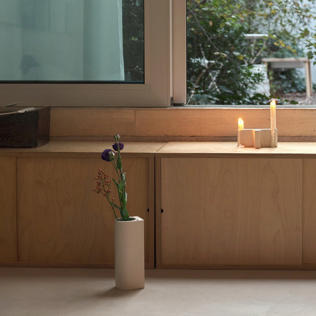 Interior view featuring white Tiili Candleholder placed on a windowsill with two candles. On the floor, white Tiili Vase holds a few branches.