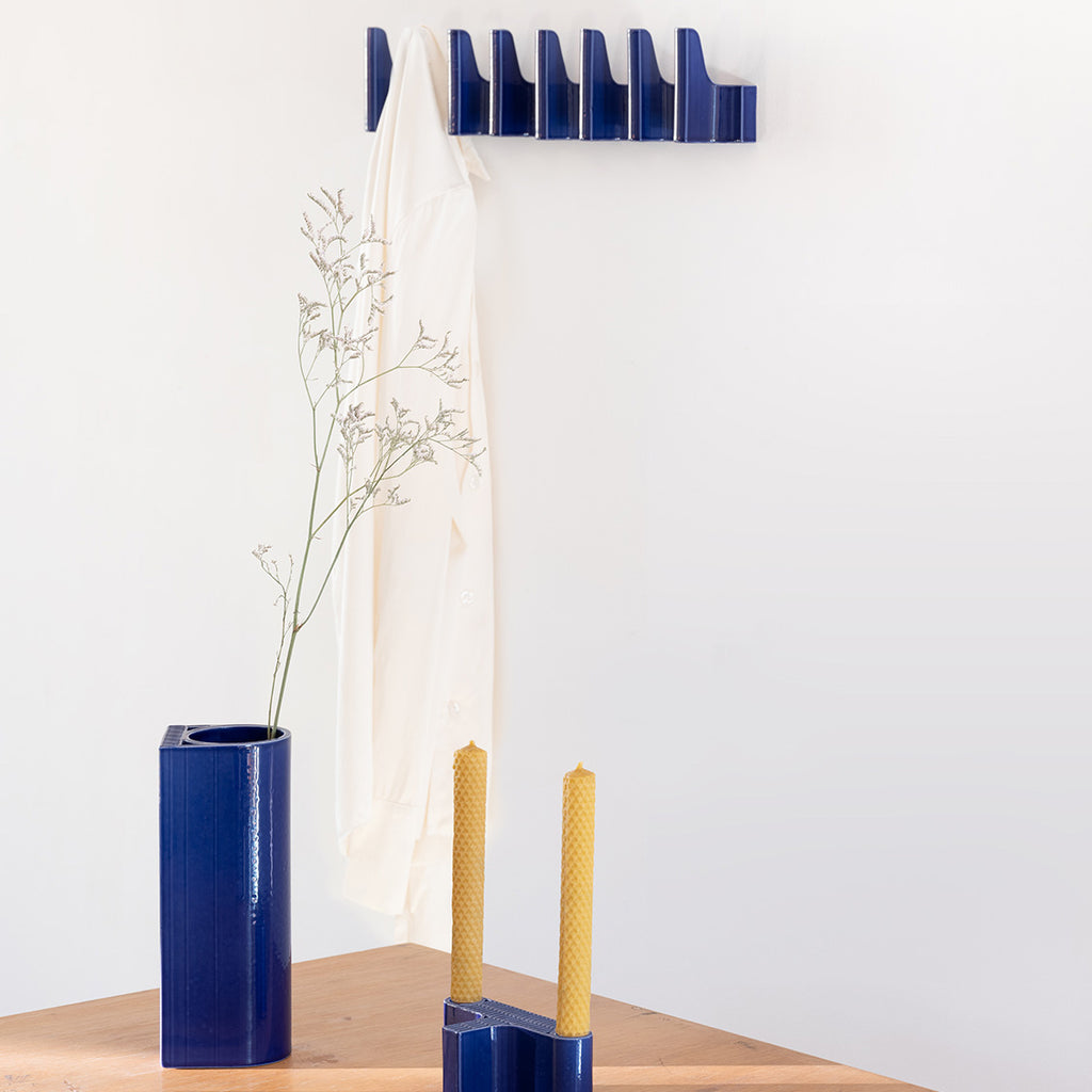 Interior view featuring dark blue Tiili collection objects. On the table, Tiili Vase and Tiili Candleholder are displayed, while multiple Tiili Wall Hooks are arranged in a row on the wall.