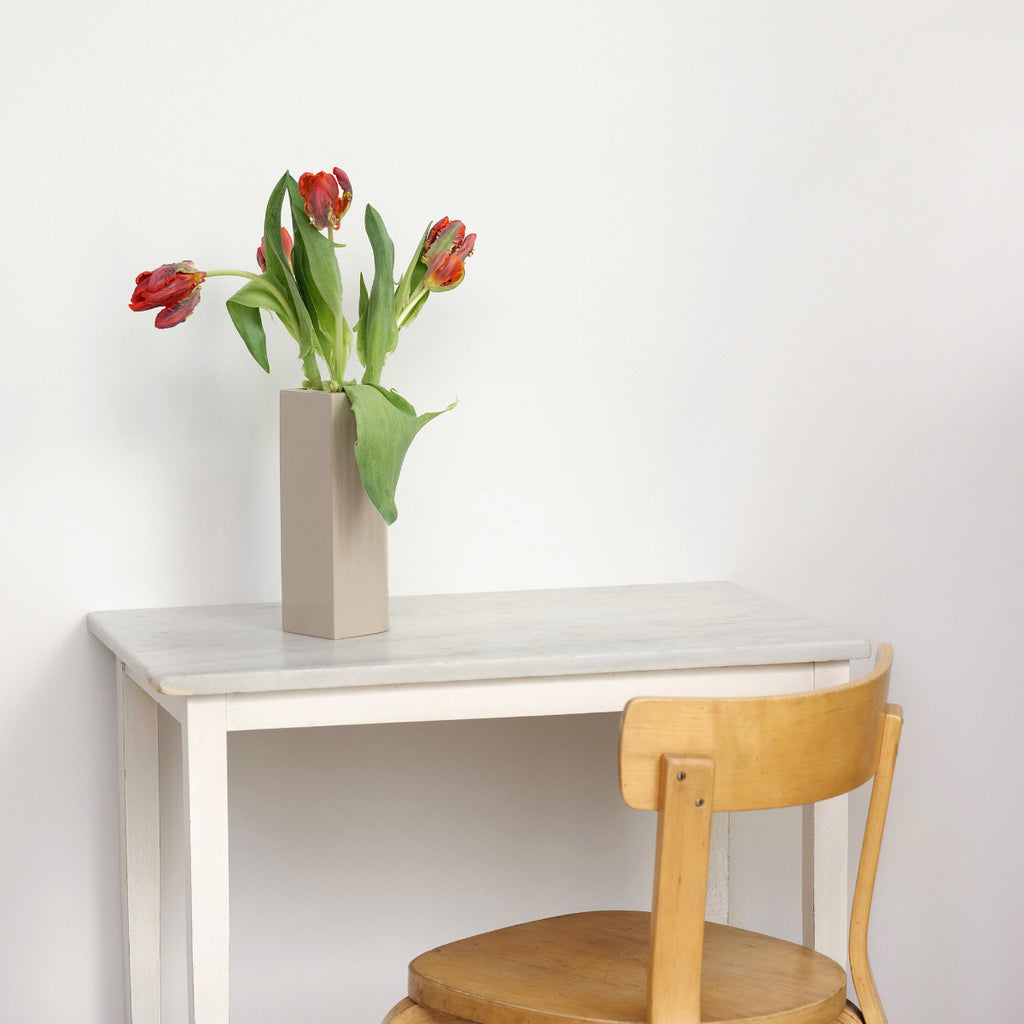 Interior view of a white room featuring a table with a green Tiili Vase holding tulips. Chair 69 is placed beside the table.